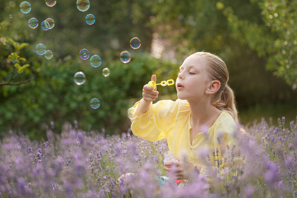 Красивая маленькая девочка ловит мыльные пузыри в поле с лавандой  - Фото, изображение