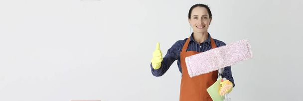 Mujer sonriente con fregona sosteniendo el pulgar hacia arriba. Recomendaciones para el concepto de empresas de limpieza - Foto, imagen