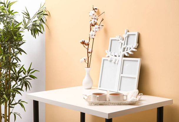 黄色の壁の近くのテーブルの上に写真フレーム、花瓶やお茶のカップで木の枝を持つ家族の木 - 写真・画像