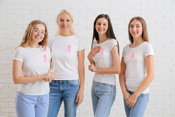 Beautiful women with pink awareness ribbons on white brick background. Breast cancer concept - Φωτογραφία, εικόνα