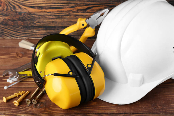 Hearing protectors with hardhat and nails on dark wooden background, closeup - Photo, Image