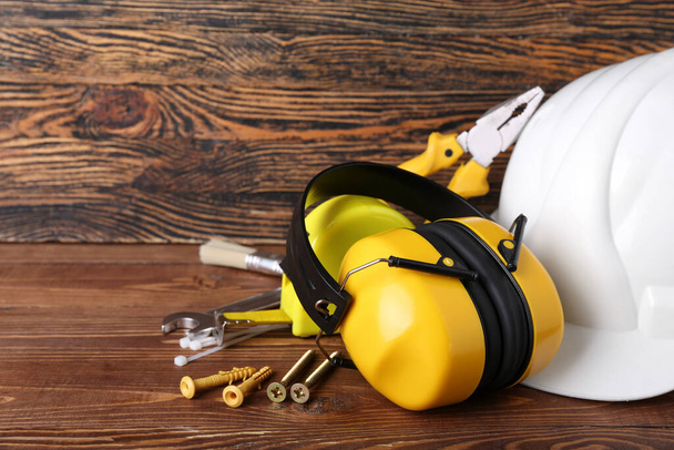 Hearing protectors with hardhat and nails on dark wooden background, closeup - Foto, Imagem