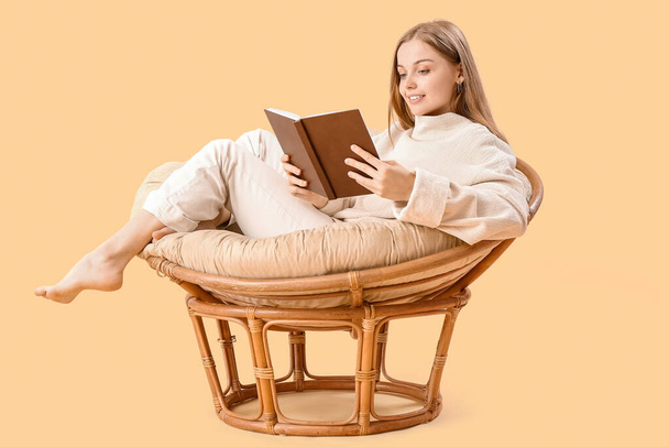 Jeune femme livre de lecture dans un fauteuil sur fond beige - Photo, image