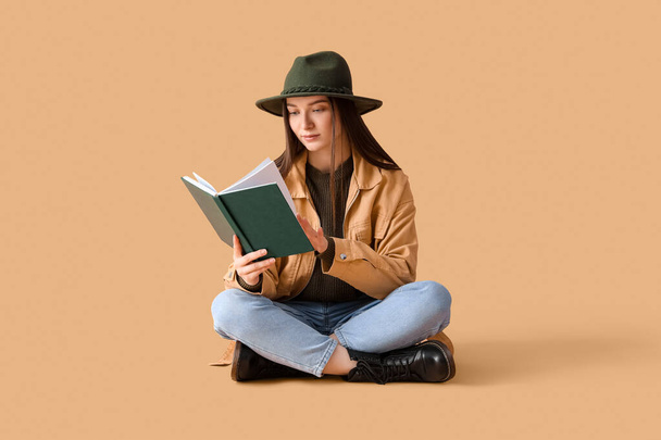 Young woman in hat reading book on beige background - Photo, Image