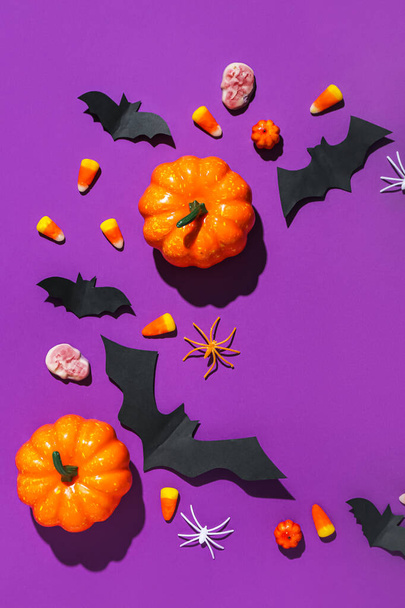 Moldura feita de guloseimas de Halloween, morcegos de papel e abóboras no fundo roxo - Foto, Imagem