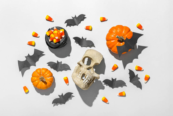 Paper bats with Halloween pumpkins, candy corns and skull on grey background - Фото, изображение