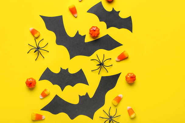 Pipistrelli di carta con dolcetti di Halloween e ragni su sfondo giallo - Foto, immagini