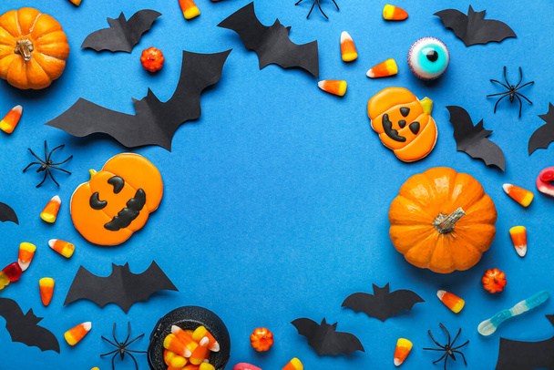 Cadre composé de friandises d'Halloween, de chauves-souris en papier et d'araignées sur fond bleu - Photo, image