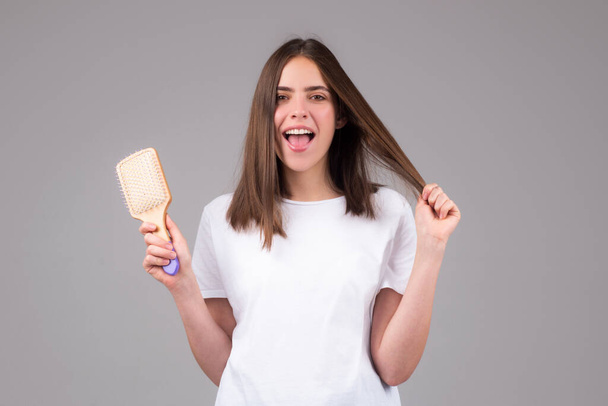 Smiling girl combing hair. Beautiful young woman holding comb straightened hair - Фото, зображення