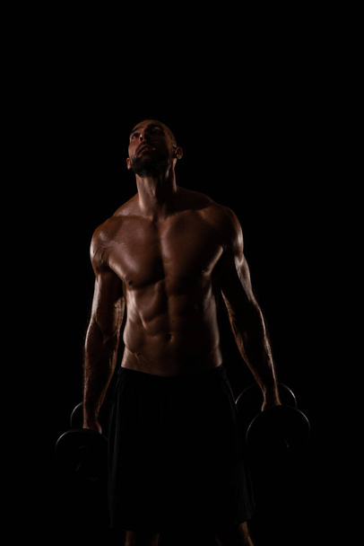 Topless and handsome guy is posing with his weights in his hands on blakc background - Foto, Bild