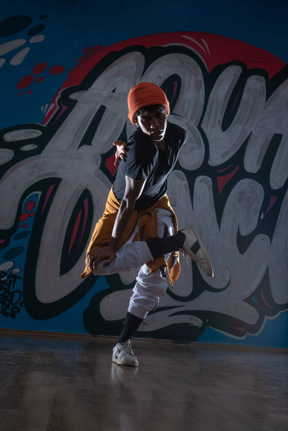 Młody czarny mężczyzna taniec hip hop styl w środowisku miejskim. ma na sobie pomarańczowy strój i jest na tle graffiti. - Zdjęcie, obraz