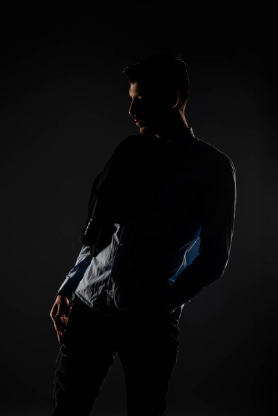 Attractive and handsome man in the studio setting himself up for the camera with a dimmed background - Photo, Image