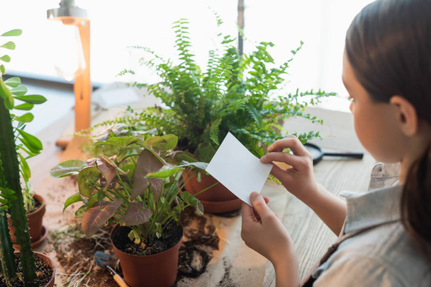 Child holding sticky note near plants and soil on table at home  - Photo, Image
