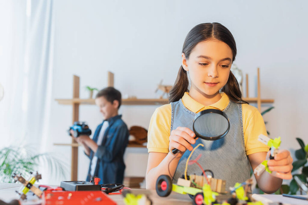 Kid holding magnifying glass and robotic model on table at home  - Photo, Image