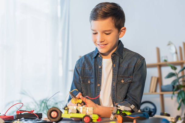 preteen boy with pliers assembling robotics model on table at home - Fotó, kép
