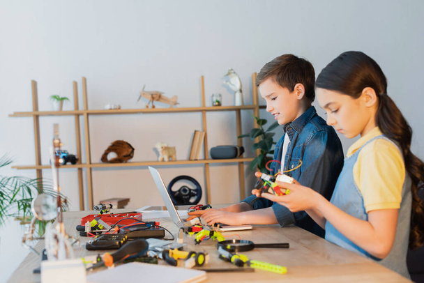 мальчик-подросток с помощью ноутбука рядом девушка держит механическую часть робототехники модели - Фото, изображение