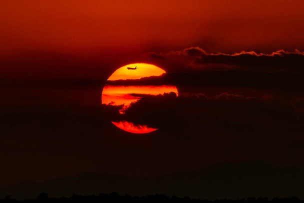 Coucher de soleil rouge partiellement obscurci par quelques nuages avec une silhouette d'avion - Photo, image