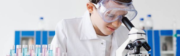 dziecko w goglach patrząc w mikroskop podczas wykonywania eksperymentu chemicznego, baner - Zdjęcie, obraz