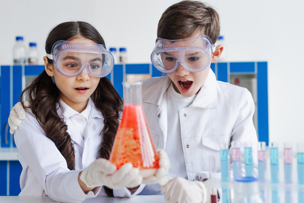 amis étonnés dans des lunettes regardant la fiole avec de la substance rouge en laboratoire - Photo, image