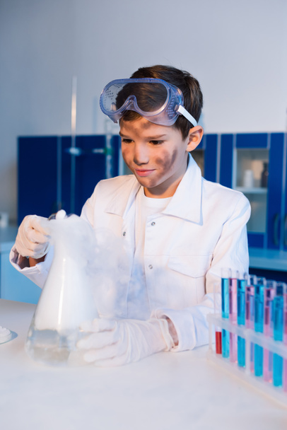 Kirli suratlı çocuk laboratuarda kimyasal deney yaparken elinde buharlı matara tutuyordu. - Fotoğraf, Görsel