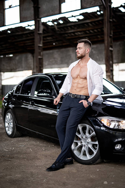Shirtless bodybuilder with black vehicle. Strong muscular man with car standing. - Fotografie, Obrázek