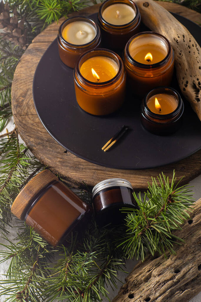 Soy candles burn in glass jars. Comfort at home. Candle in a brown jar. Scent and light. Scented handmade candle. Aroma therapy. Christmas tree and winter mood. Cozy decor. Festive decoration - Φωτογραφία, εικόνα