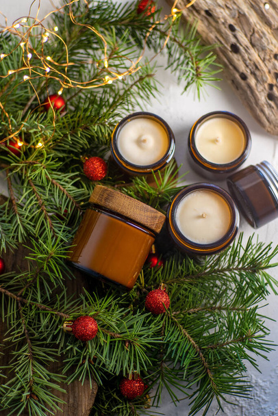 Soy candles burn in glass jars. Comfort at home. Candle in a brown jar. Scent and light. Scented handmade candle. Aroma therapy. Christmas tree and winter mood. Cozy decor. Festive garland decoration - Valokuva, kuva