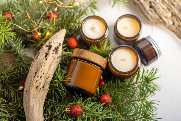 Soy candles burn in glass jars. Comfort at home. Candle in a brown jar. Scent and light. Scented handmade candle. Aroma therapy. Christmas tree and winter mood. Cozy decor. Festive garland decoration - Fotografie, Obrázek