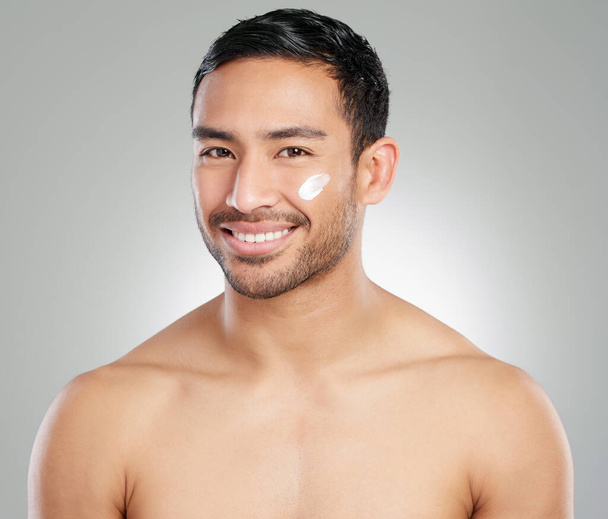 Healthy skin, happy guy. Studio shot of a handsome young man applying moisturiser against a grey background - Φωτογραφία, εικόνα
