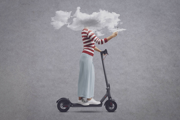 Woman with head in a cloud riding a scooter and using her smartphone, social media addiction and nomophobia concept - Foto, Imagem