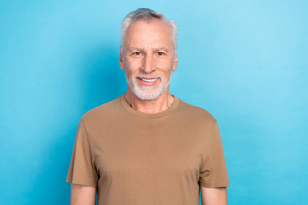 Photo of glad pleasant cheerful pensioner man with gray hairstyle stubble wear beige t-shirt smiling isolated on blue color background. - Fotó, kép