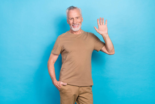 Photo of good looking man dressed fashionable trendy outfit raise arm demonstrate hi symbol isolated on blue color background. - Photo, image
