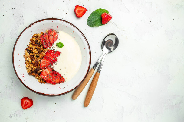 Granola with yogurt with fresh strawberry, chia seeds and honey on a white background. Delicious balanced food concept. banner, menu, recipe place for text, top view. - Valokuva, kuva