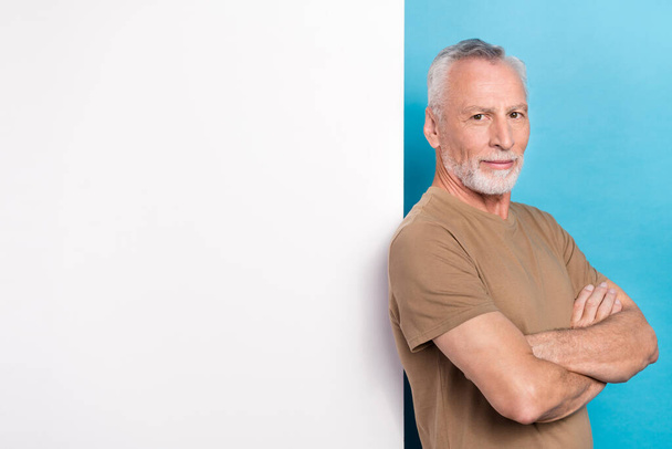 Photo of positive handsome senior man with gray hairstyle stubble wear beige t-shirt hands folded isolated on blue color background. - Foto, Bild