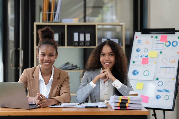 Een glimlachende jonge zwarte zakenvrouw die samenwerkt met een collega op kantoor. financieel concept - Foto, afbeelding