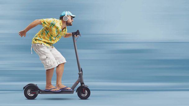Cool stylish man wearing a colorful beach shirt and riding a fast eco-friendly electric scooter, smart mobility concept - Фото, зображення