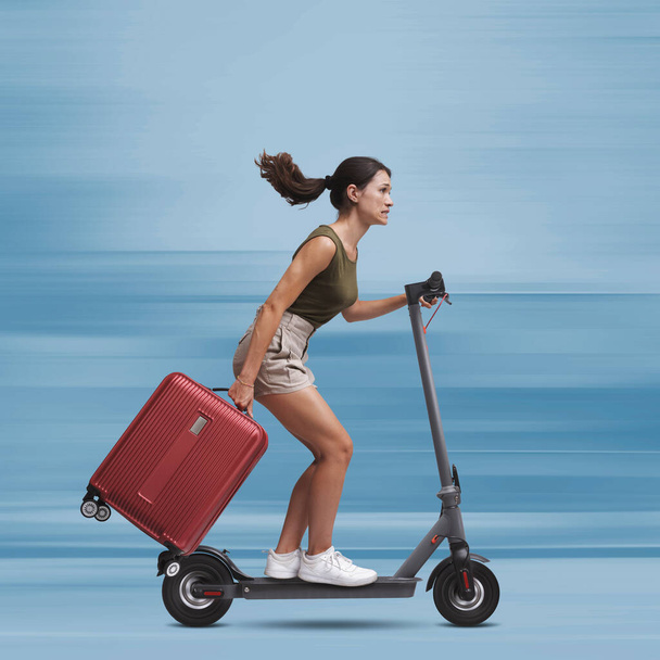 Turistka na rychlém elektrickém skútru a nesoucí tašku na vozíku, má zpoždění, koncept udržitelné mobility - Fotografie, Obrázek