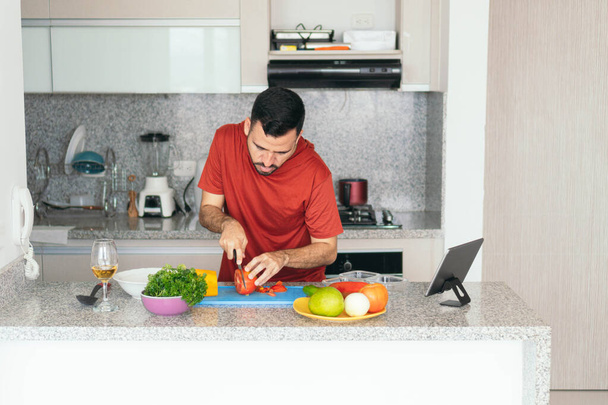 Γενειοφόρος άντρας κάνει μια βιντεοκλήση ενώ μαγειρεύει στο σπίτι - Φωτογραφία, εικόνα