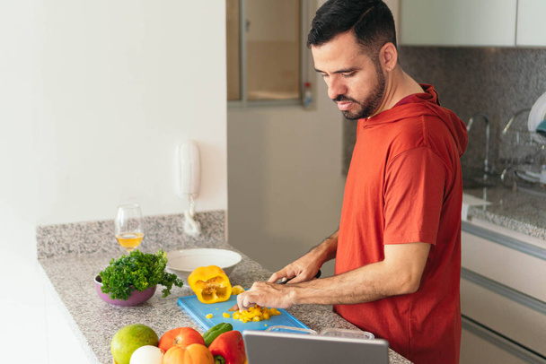 Hombre Hispano haciendo una videollamada mientras cocina en la casa - Foto, imagen