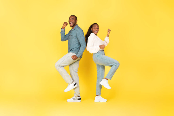 Vreugdevol Afro-Amerikaans paar Gesturing Ja Vieren Groot Succes poseren Staande op gele Studio Achtergrond. Vreugde en zegeviering Concept. Volledige lengte schot - Foto, afbeelding