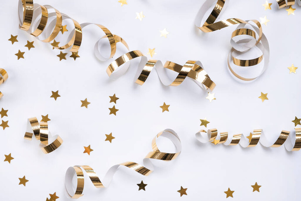 flat composition of golden ribbons or serpentine and golden confetti in the form of stars on a white background. The concept of a birthday, anniversary or holiday in golden colors. - Foto, afbeelding