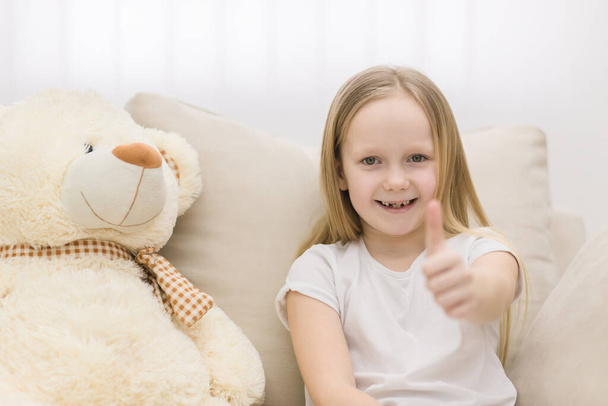 Photo of teddy bear and little girl showing thumb up at the camera. Concept of cute little girl. - Φωτογραφία, εικόνα
