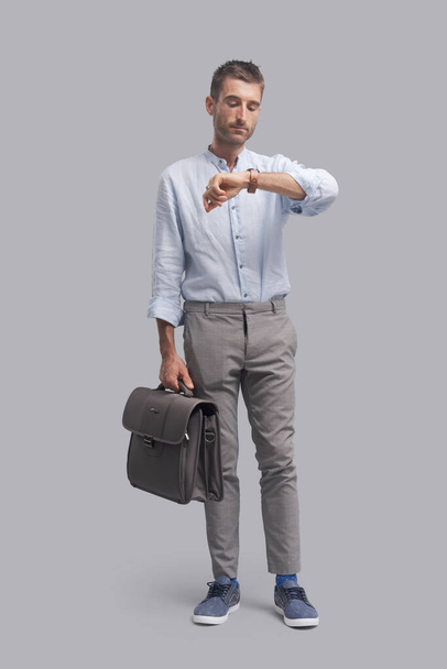 Corporate businessman standing and holding a briefcase, he is checking the time and waiting for a meeting - Foto, Imagen