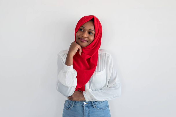 Задумчивая американка-мусульманка из Африки думает и смотрит в сторону на свободное пространство, стоя на фоне белой стены. Дайте мне подумать об этом концепции - Фото, изображение