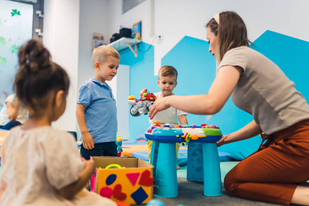 kids and a teacher sitting on the circle on the floor and playing with plastic toys, kindergarten games for preschoolers. High quality photo - Valokuva, kuva