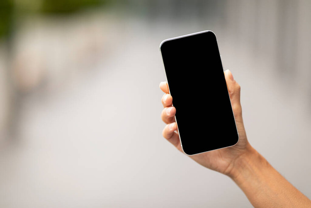 Неузнаваемая женщина держит в руках современный смартфон с черным пустым экраном, макет, избирательный фокус на мобильный телефон, размытый фон, панорама с копировальным пространством, мобильное приложение, онлайн-предложение, концепция - Фото, изображение