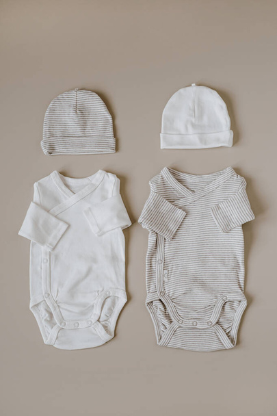 Elegante Babyanzüge und Hüte auf neutralem pastellbeigem Hintergrund. Flache Lage, Draufsicht - Foto, Bild