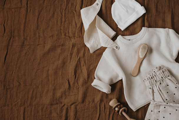 Cute elegant stylish Scandinavian newborn baby clothes and accessories. Online fashion store, online shopping branding concept. Sweater, joggers, hat, muslin bib on brown muslin blanket - Photo, Image