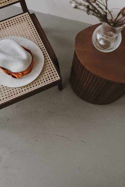 Eleganter stilvoller Rattanstuhl, getrockneter Blumenstrauß, Hut, Beistelltisch. Moderne ästhetische minimalistische Wohnzimmereinrichtung. Luxus-Wohnung Innenausstattung Details. Blick von oben - Foto, Bild
