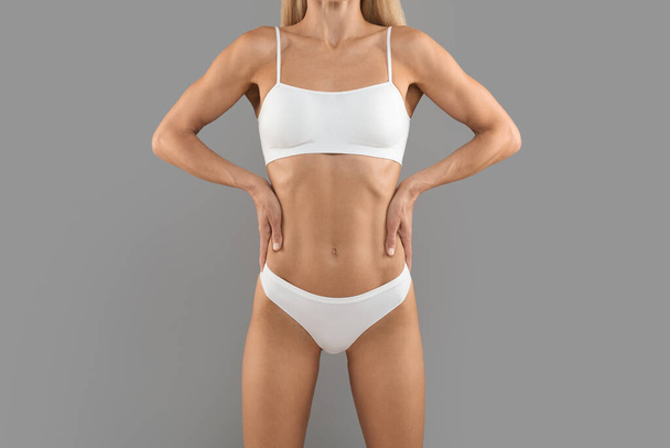 Концепция похудения. Обрезанный снимок спортивного стройного женского тела в нижнем белье, неузнаваемая молодая женщина с идеальной спортивной фигурой, стоящая с руками на талии на сером фоне, скопировать пространство - Фото, изображение